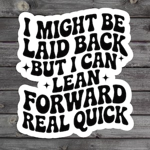May include: White sticker with black text that reads "I MIGHT BE LAID BACK BUT I CAN LEAN FORWARD REAL QUICK." The sticker has a retro font and is on a wooden background.