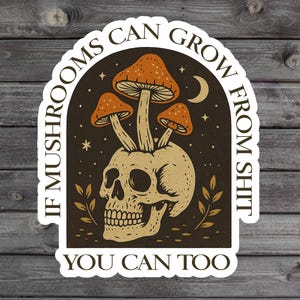 May include: A sticker featuring a skull with orange mushrooms growing from its head. The sticker has the text "IF MUSHROOMS CAN GROW FROM SHIT YOU CAN TOO" in a curved font, with a dark brown background.