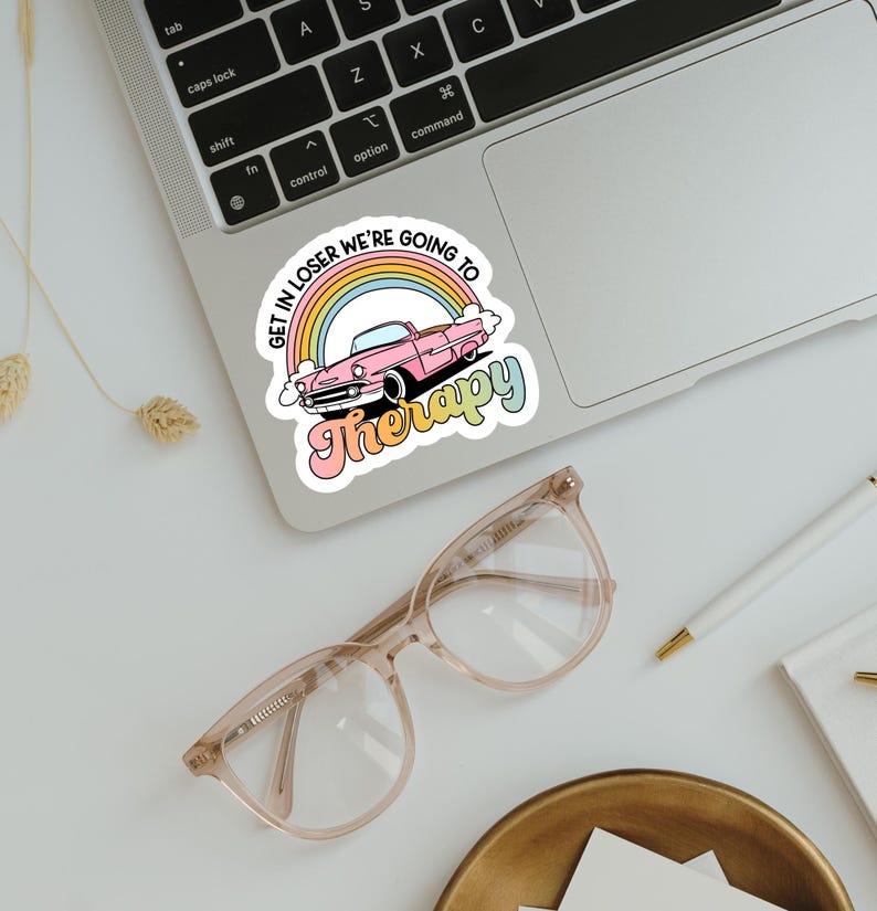 Pu&ograve; includere: Un adesivo con la scritta "GET IN LOSER WE'RE GOING TO Therapy" in un font retr&ograve;. L'adesivo presenta un'auto rosa classica davanti a un arcobaleno. L'adesivo &egrave; su un laptop.