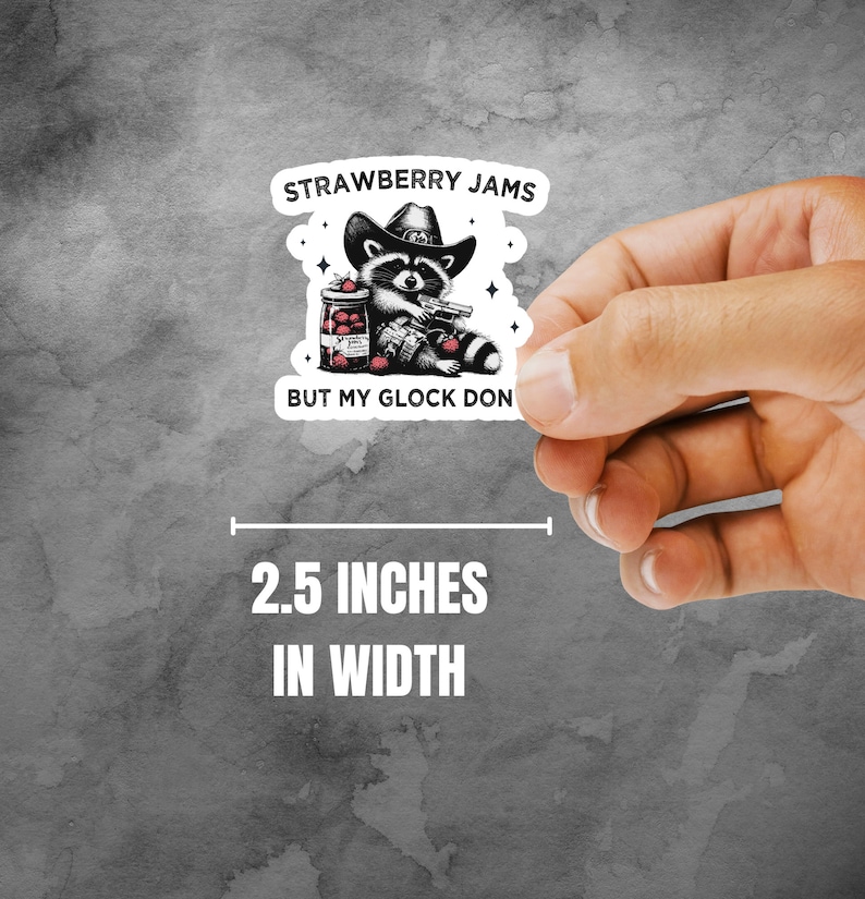 May include: A black and white illustration of a raccoon wearing a cowboy hat and holding a jar of strawberry jam and a gun. The text reads "Strawberry Jams But My Glock Don". The sticker is 2.5 inches wide.