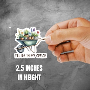 May include: A sticker featuring a watercolor illustration of a wheelbarrow filled with potted plants. The sticker is 2.5 inches in height and has the text "I'LL BE IN MY OFFICE". The wheelbarrow is teal with a silver handle.