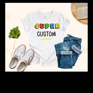 May include: White t-shirt with the text "SUPER CUSTOM" in colorful block letters and five yellow stars.