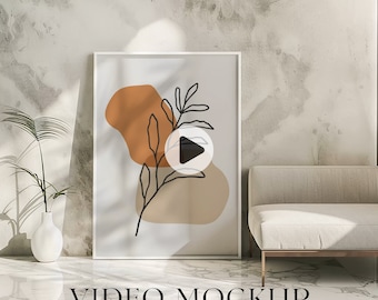 May include: A white framed poster with a minimalist abstract design featuring a brown and beige organic shape with a black line drawing of a branch with leaves. The poster is hanging on a white wall with a white couch in the foreground. The text "VIDEO MOCKUP" is at the bottom of the image.