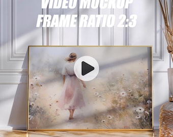 May include: A framed artwork with a gold border, depicting a woman in a pink dress walking through a field of white flowers. The artwork is displayed on a wooden floor against a white wall. Text at the top reads "VIDEO MOCKUP FRAME RATIO 2:3".