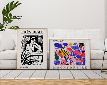 Könnte beinhalten: Zwei gerahmte Kunstdrucke auf einem weißen Sofa. Der Druck auf der linken Seite ist schwarzweiß und zeigt eine Frau, die in einem Garten sitzt. Der Text auf dem Druck lautet "TRÈS BEAU" und "Franch". Der Druck auf der rechten Seite ist bunt und zeigt abstrakte Formen und den Text "SIMPLE" und "MOCKTOPTIRE".