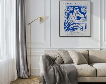 Könnte beinhalten: Ein schwarzer gerahmter Poster mit einer blauen Illustration einer Frau, die in einem Garten sitzt. Der Poster hat den Text "SIMPLE Frame mockup" und "FOR SMART OBJECT MOCKTOPTIRE" darauf. Der Poster hängt an einer weißen Wand über einem beigen Sofa mit einer grauen Wolldecke.