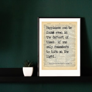 Può includere: Stampa incorniciata con la citazione "La felicità può essere trovata anche nei momenti più bui, se ci si ricorda solo di accendere la luce". Il testo è in nero su uno sfondo di giornale vintage.