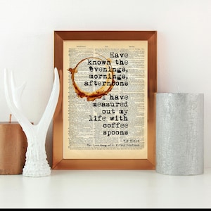 Könnte beinhalten: Ein gerahmter Druck mit einem Kaffeefleck-Design und dem Zitat "Have known the evenings, mornings, afternoons. I have measured out my life with coffee spoons." Dekorative Kerzen und eine weiße Geweihskulptur sind ebenfalls im Bild.