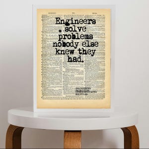 Può includere: Una stampa incorniciata con uno sfondo di una pagina di dizionario vintage con il testo nero: Engineers solve problems nobody else knew they had. Sotto, un testo più piccolo recita: ENGINEERING UNCOMPLICATED SOLUTIONS. La cornice è bianca.