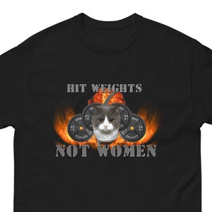 Könnte beinhalten: Schwarzes T-Shirt mit einem Katzenkopf und Hanteln, vor einem feurigen Hintergrund. Der Text "HIT WEIGHTS NOT WOMEN" ist über und unter dem Katzenbild aufgedruckt. Das Shirt ist aus weichem Material.