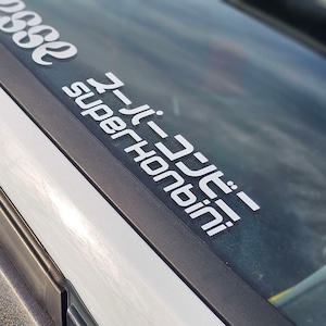 Puede incluir: Una pegatina de vinilo blanca con el texto "Super Hontini" y "J-Tuned" en caracteres japoneses sobre un fondo negro.