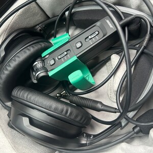 May include: Black headphones with a green and black microphone and a black carrying case. The microphone has a label that says "Bose".