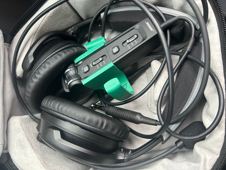 May include: Black headphones with a green and black microphone and a black carrying case. The microphone has a label that says "Bose".