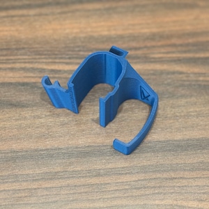 May include: A blue plastic cable clip with a small arrow on the side. The clip is designed to hold cables in place.