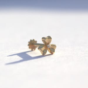 May include: A gold nose ring with a small diamond in the center of a four-leaf clover design.