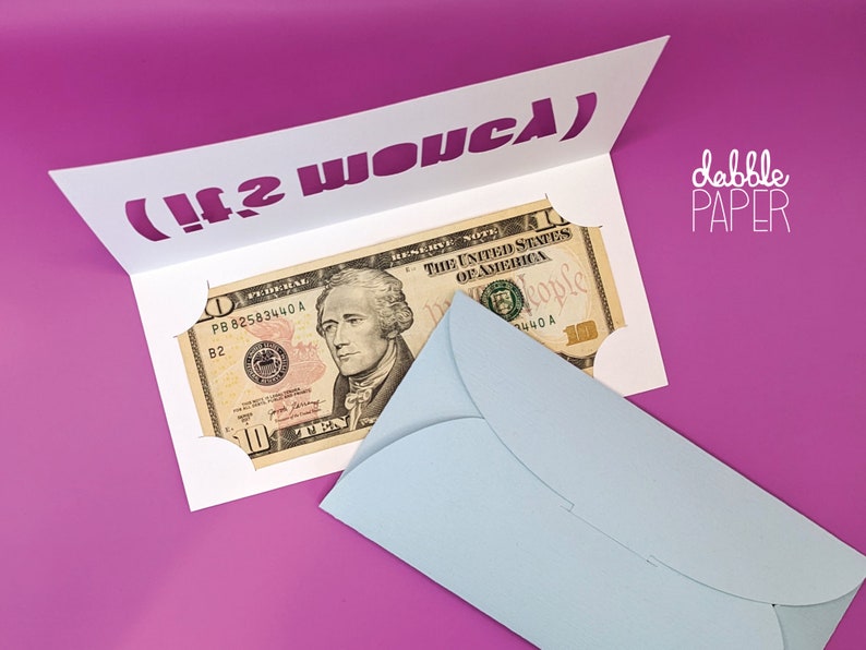 May include: A white card with a cut-out slot for money. The card has the text "(It2 WO&upsilon;&sigmaf;&lambda;)" printed in purple. A ten dollar bill is inserted into the slot. A light blue envelope is on the right side of the card.