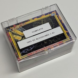 May include: A clear plastic case containing a complete set of 1993 DC Bloodlines trading cards. The cards are stacked neatly inside the case, with a white label reading "COMPLETE" and "1993 DC BLOODLINES 1-81". The cards have colorful artwork.