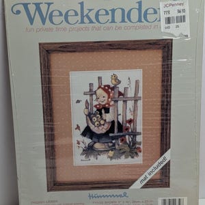May include: A framed cross-stitch kit titled "Weekender" featuring a Hummel design. The artwork depicts a child with a basket, a fence, and a bird. The finished size is 5 x 7 inches.
