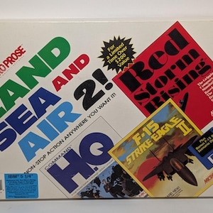 May include: A vintage computer game box featuring the titles "Land, Sea and Air 2!" and "Red Storm Rising." The box includes graphics of an F-15 Strike Eagle II and a HQ Command game. The box is white with colorful text.