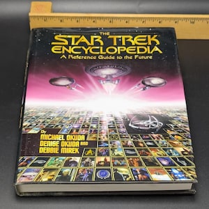 May include: The Star Trek Encyclopedia book with a black cover and the title in yellow and white. The cover features images of Star Trek ships and a grid of images. The book is a reference guide to the future, written by Michael Okuda, Denise Okuda, and Debbie Mirek.