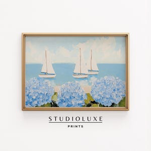May include: A framed horizontal art print featuring an oil painting of three white sailboats on a light blue sea under a pale sky, with large clusters of textured light blue hydrangea flowers in the foreground. The text STUDIOLUXE PRINTS appears below.