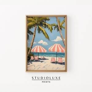 May include: Framed beach scene print featuring palm trees, a sandy shore, and two striped umbrellas. Several beach chairs are visible under the umbrellas. The sky is blue with fluffy white clouds. The text "STUDIOLUXE PRINTS" is at the bottom.
