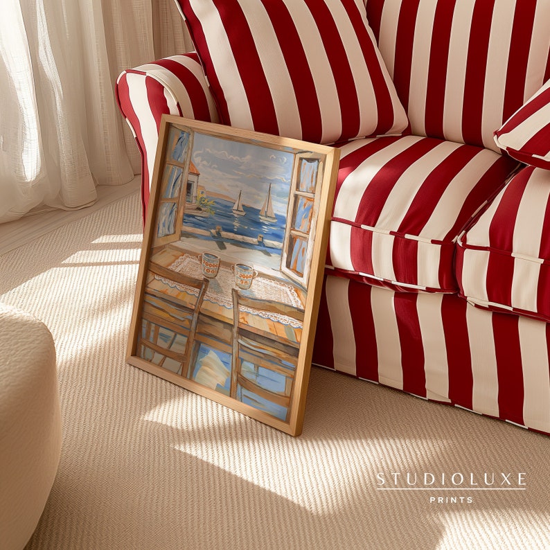 May include: A framed painting of a seascape with boats and a building in the distance. The painting is in a wooden frame and is sitting on a red and white striped couch.