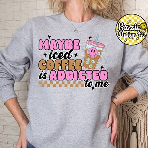 Puede incluir: Sudadera gris con el texto "Maybe iced coffee is addicted to me" en letras rosas y negras. Un vaso de caf&eacute; helado de dibujos animados con una cara sonriente est&aacute; al lado del texto.