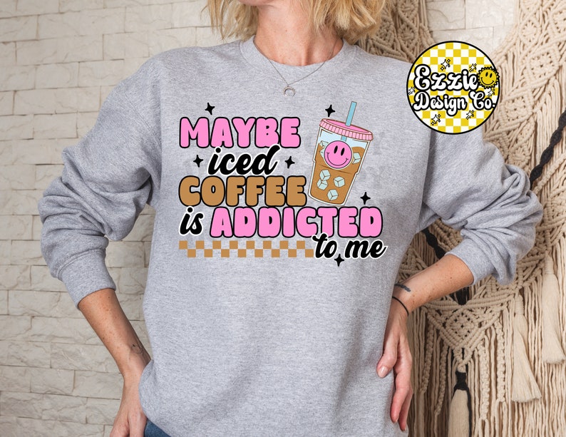 Puede incluir: Sudadera gris con el texto "Maybe iced coffee is addicted to me" en letras rosas y negras. Un vaso de caf&eacute; helado de dibujos animados con una cara sonriente est&aacute; al lado del texto.