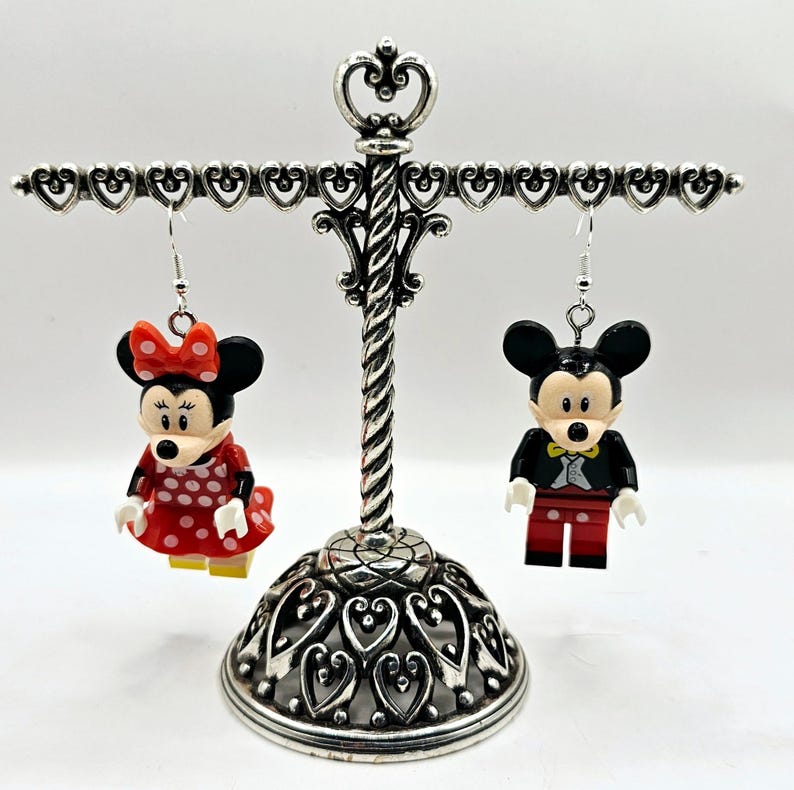 May include: A pair of dangle earrings featuring a red and white polka dot Minnie Mouse and a black and red Mickey Mouse. The earrings are hanging from a silver earring stand.