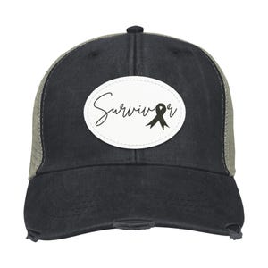 May include: Black and gray trucker hat with a distressed finish. The front features a white oval patch with the word "Survivor" in script and a black ribbon graphic. The mesh back is a light gray color.