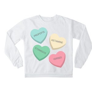 May include: White sweatshirt with four candy hearts printed on the front. The hearts are in different colors and have the words "PROPOFOL", "KETAMINE", "ETOMIDATE", and "VERSED" printed on them.