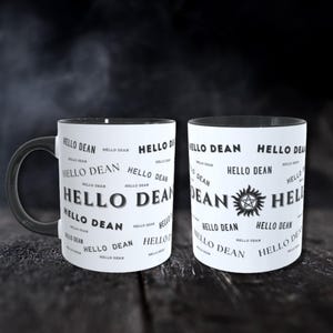 Könnte beinhalten: Zwei weiße Keramikbecher mit schwarzen Rändern. Ein Becher hat ein schwarz-weißes Design mit dem Text "HELLO DEAN", der mehrmals wiederholt wird. Der andere Becher hat das gleiche Design mit einem zusätzlichen schwarz-weißen Symbol in der Mitte.