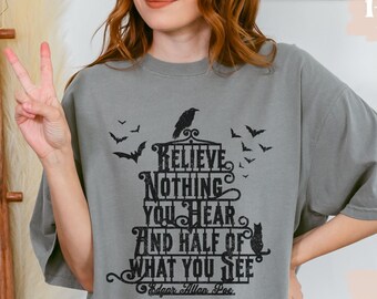 Puede incluir: Camiseta gris con un estampado gráfico negro de una casa encantada con murciélagos y un cuervo. El texto en la casa dice "No creas nada de lo que escuches y la mitad de lo que veas" con "Edgar Allan Poe" en la parte inferior.