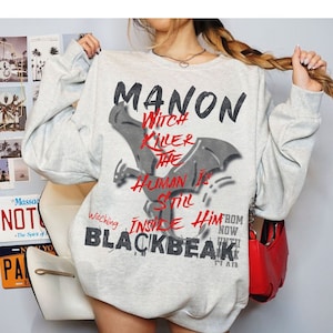 Puede incluir: Una sudadera gris con un estampado gráfico de un murciélago y el texto "MANON Witch Killer The Human Is Still Inside Him From Now Until Blackbeak".