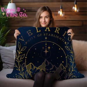K&ouml;nnte beinhalten: Eine marineblaue Kuscheldecke mit goldener Aufschrift "Velaris City of Starlight". Die Decke zeigt eine goldene Illustration einer Bergkette mit Sternen und einem Halbmond.