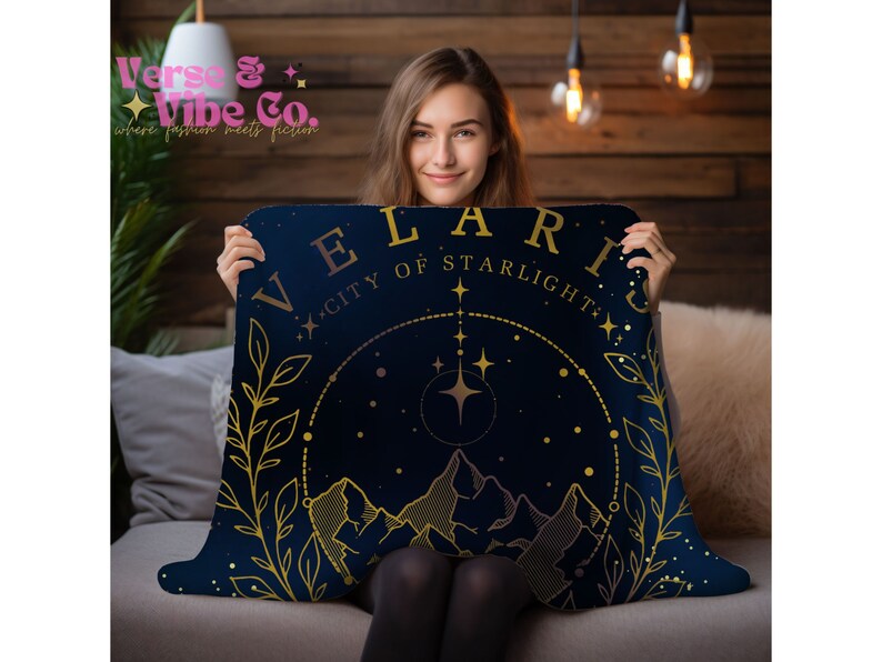 K&ouml;nnte beinhalten: Eine marineblaue Kuscheldecke mit goldener Aufschrift "Velaris City of Starlight". Die Decke zeigt eine goldene Illustration einer Bergkette mit Sternen und einem Halbmond.