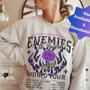 May include: Gray sweatshirt with a purple and black graphic design that says "Enemies to Lovers World Tour" with a purple rose and flames. The text "Book Addicts Anonymous Presents" is at the top of the graphic. The sweatshirt is available as a sweatshirt.