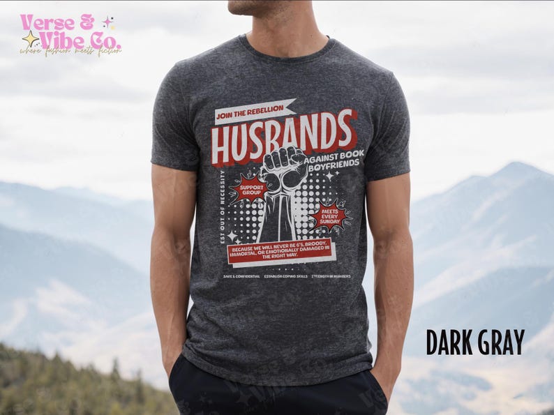 以下が含まれることがあります： ダークグレーのTシャツに、「Join the Rebellion: Husbands Against Book Boyfriends」というグラフィックプリントが施されています。グラフィックには、握りこぶしがあげられ、「Est out of necessity, Support Group, Meets Every Sunday, Because we will never be it's broody, hormonal, or emotionally damaged in the right way.」というテキストが書かれています。