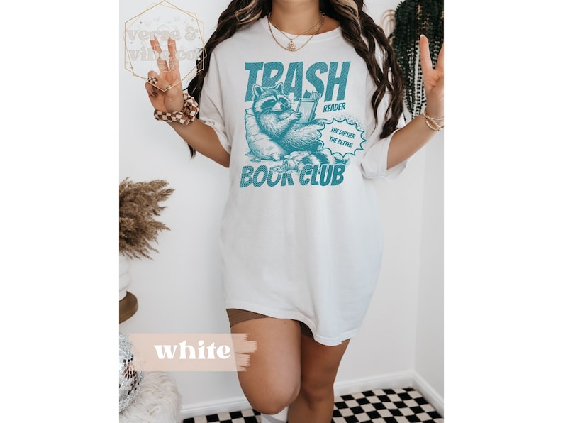 Puede incluir: Camiseta blanca con un gr&aacute;fico de un mapache leyendo un libro. El gr&aacute;fico dice "Trash Reader" y "The dirtier the better" con "Book Club" debajo.