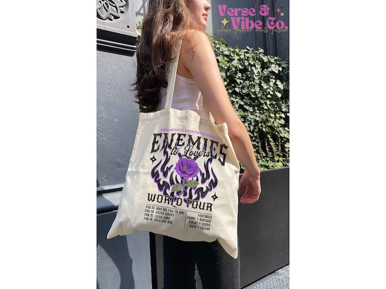 May include: A white canvas tote bag with a purple and black graphic design featuring a rose and the text "Enemies to Lovers World Tour".