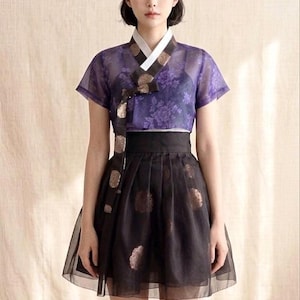 May include: A two-piece outfit consisting of a short-sleeved purple sheer blouse with a floral pattern and a white collar, paired with a high-waisted black skirt featuring a sheer overlay and circular metallic gold-toned patterns on the fabric.