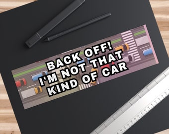 May include: A black and white bumper sticker with the text "Back Off! I'm Not That Kind Of Car" on a background of a city street with cars.