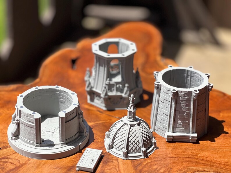 May include: A collection of gray miniature architectural models, including a domed roof, cylindrical towers, and a small rectangular door. The models are arranged on a wooden surface, showcasing intricate details and textures.