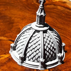 May include: A gray, 3D-printed architectural model of a domed structure with a detailed roof and a spire. The model features intricate detailing and a textured surface, showcasing a miniature replica of a building.