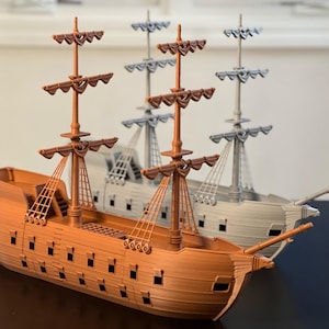 May include: Two wooden model ships, one brown and one grey, with intricate details and sails. The ships are on a dark surface.