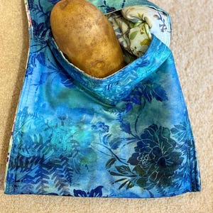 May include: A blue and green floral fabric bag with a brown potato inside.