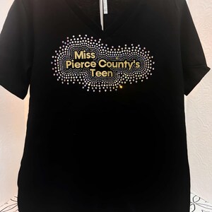 Puede incluir: Camiseta negra de cuello en V con un dise&ntilde;o de purpurina dorada que dice "Miss Pierce County's Teen".