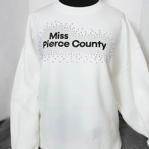 May include: White sweatshirt with a black graphic that says "Miss Pierce County" surrounded by iridescent rhinestones.