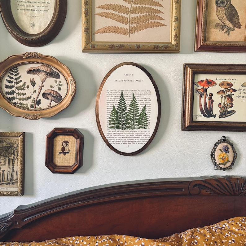 May include: A collection of framed botanical and nature-themed art pieces. The frames vary in shape and size, with gold and brown tones. The artwork includes fern prints, mushroom illustrations, and an owl. One frame has the text "AN UNEXPECTED PARTY".